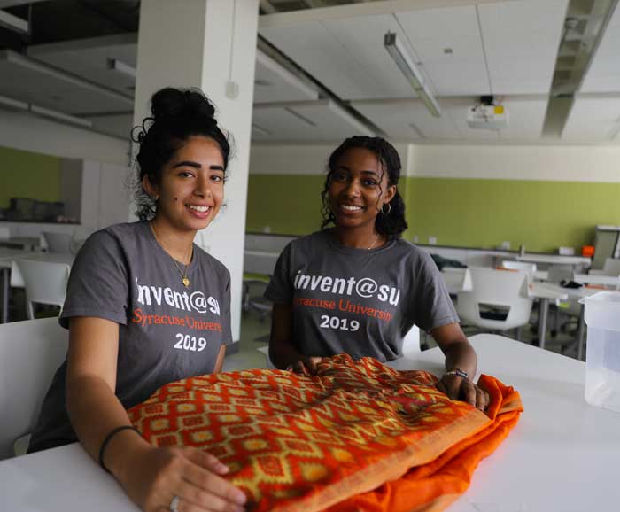 Two students pose next to a sari on a table