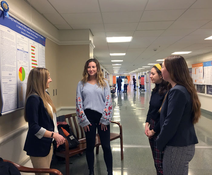 Students talk in hall in front of a winning research poster