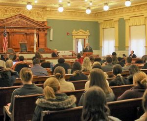 A group of people listen to a speaker in a courtroom