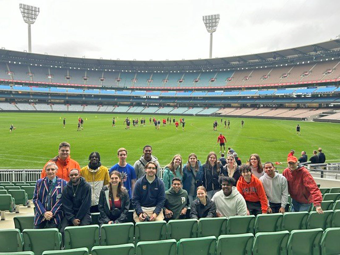 A group of people are posed in a rugby stadium during a game.