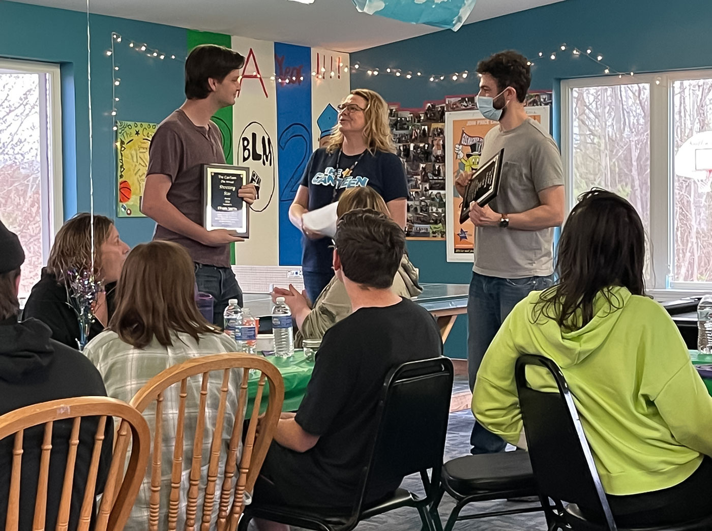 Two young males hold plaques in a room of young people