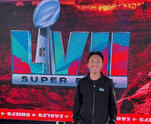 Alex Goo stands in front of a Live Super Bowl screen