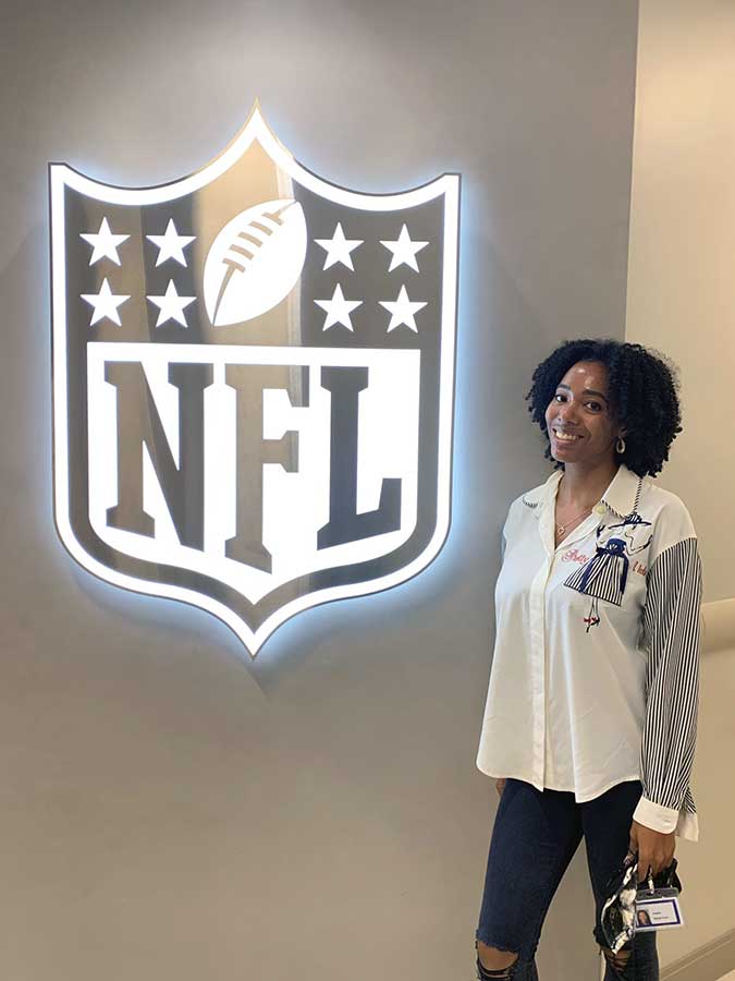 Angela Marsh-Coan poses in front of an NFL logo sign