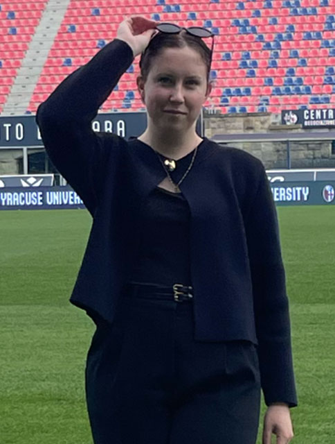 Anna Meara Pierce standing on athletic field holding her glasses on her head