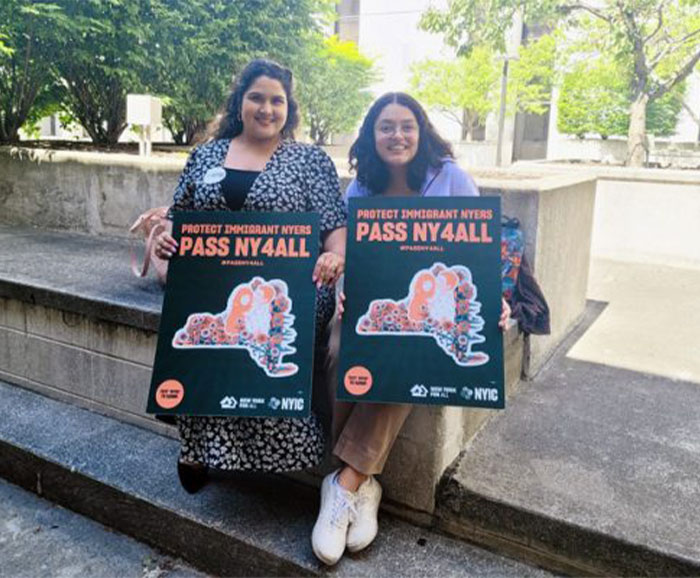 Two young women hold signs that say Pass NY 4 All.