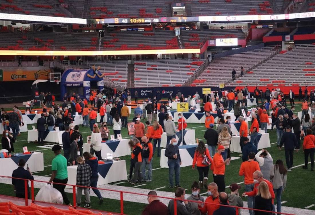 Many people wander around tables set up in a sports stadium