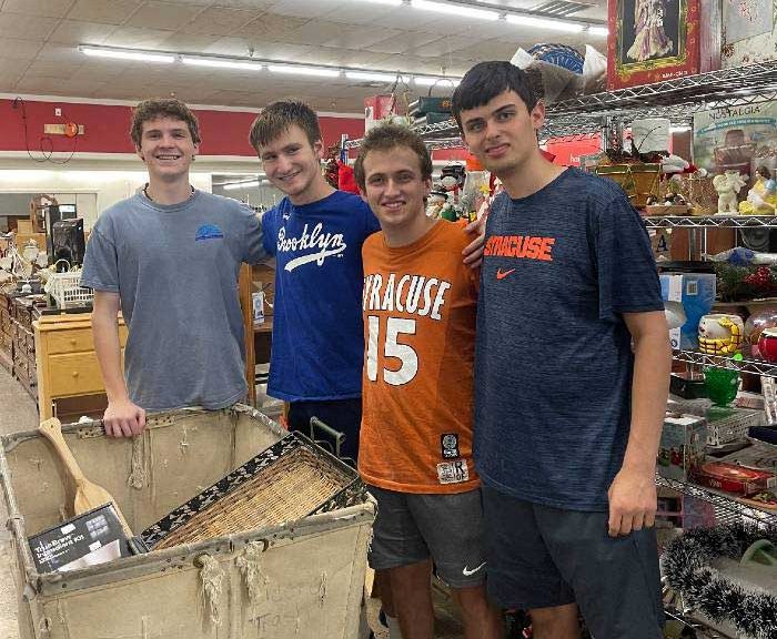 Four male students are posed in a thrift shop with a large cart