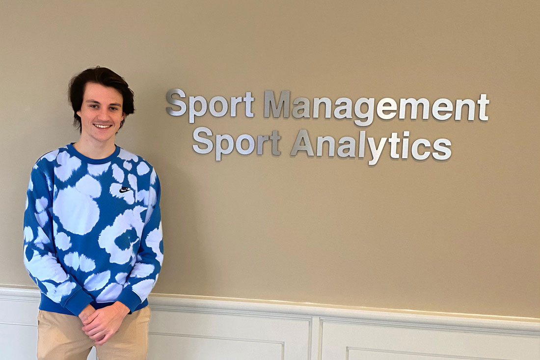 Austin Murphy stands next to a Sport Management, Sport Analytics sign