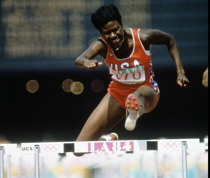women running hurdles in olympics, wearing orange USA track suit