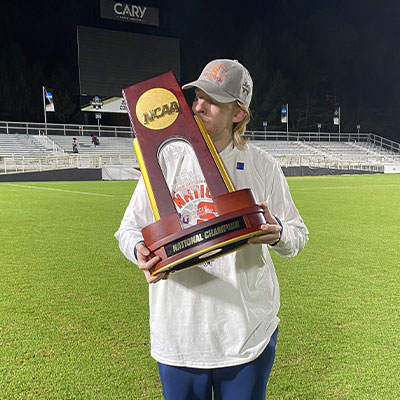 Sean Bolan stands on a soccer field with a trophy