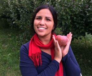 Briana Alfaro holds a fresh apple in an orchard