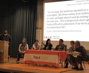 A panel of 6 sit around a table on a stage