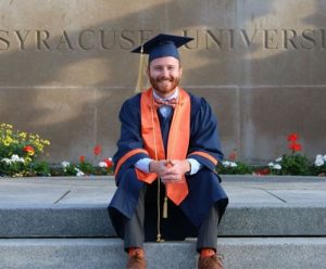Connor Howard poses with graduation gown on campus