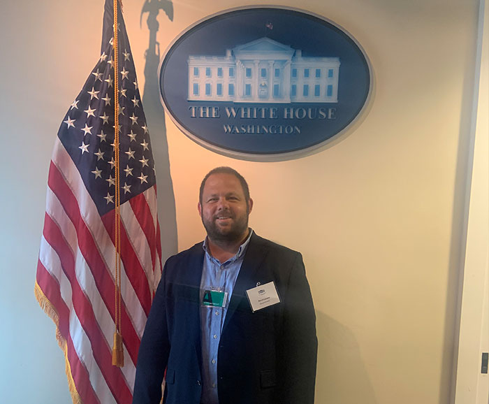 David Larsen standing under oval sign that reads