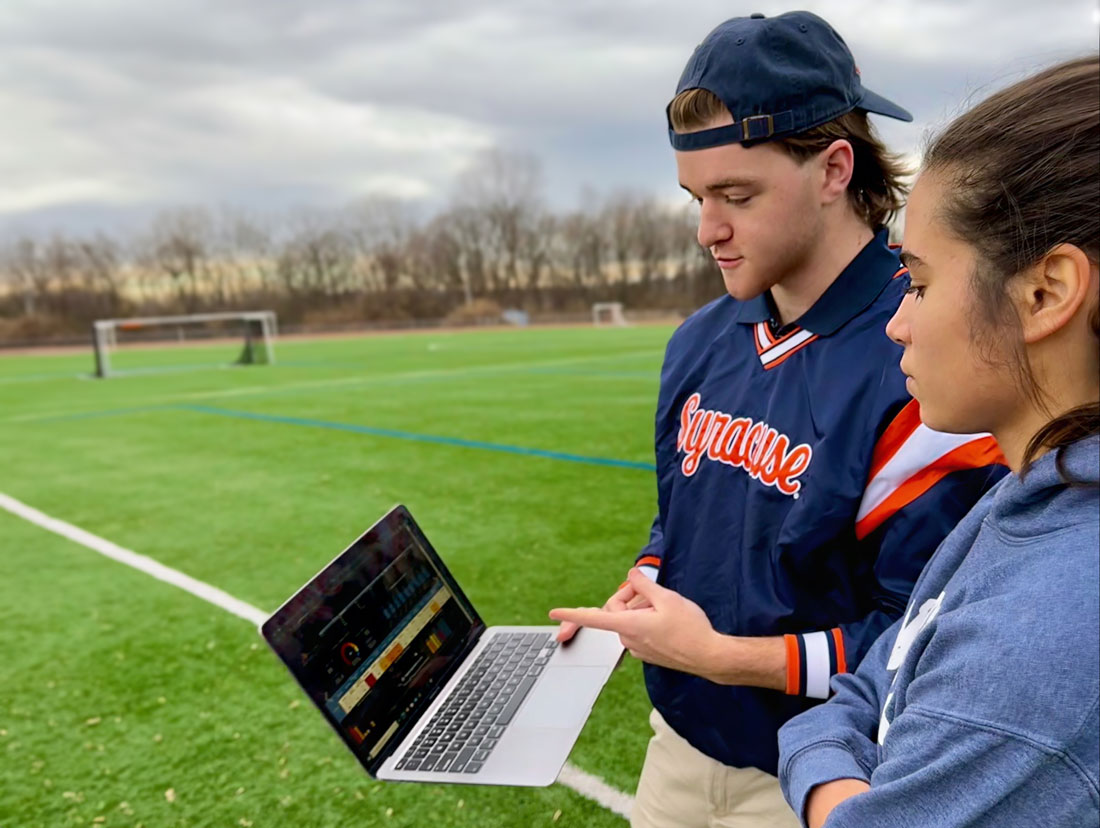 Two students in a soccer field study a laptop screen