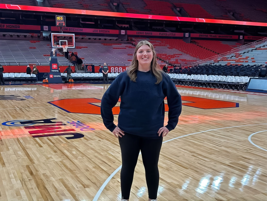 A women stands in the middle of a basketball court in a large stadium.