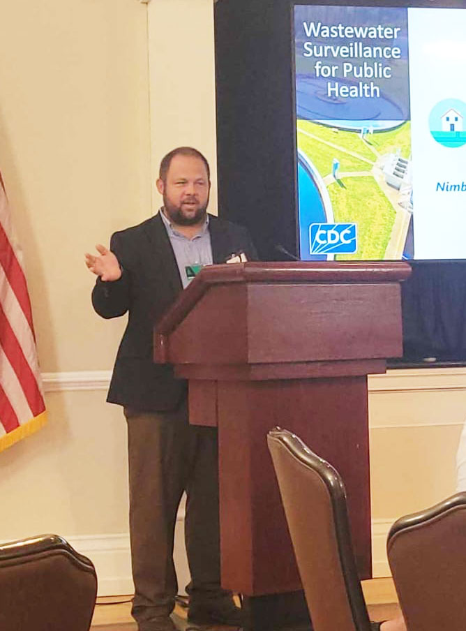 man standing behind a podium presenting about wastewater surveillance for public health