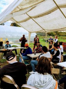 A person presents to an audience under an outdoor tent