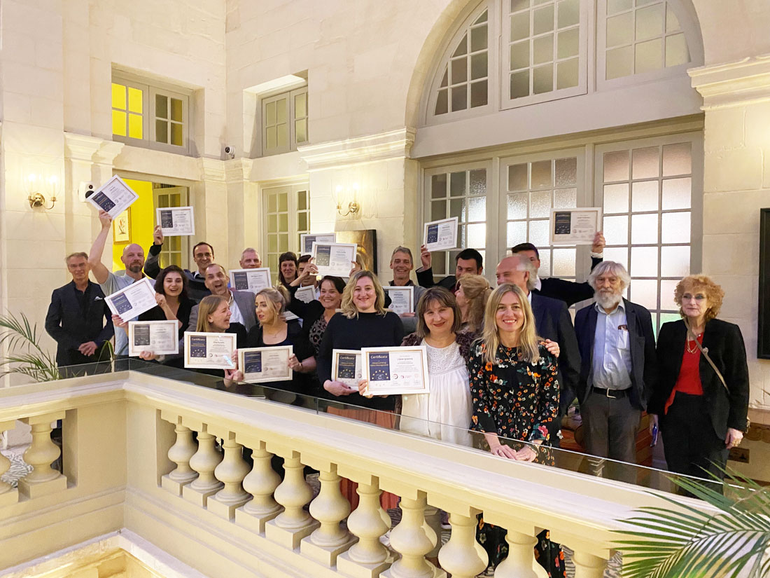 A large group of people are posed on a stairwell holding certificates