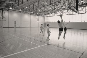 A 1980s photo of 4 men playing basketball in a gym.