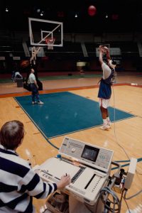 A 1990s photo of a researcher with a machine hooked up to a student shooting hoops.