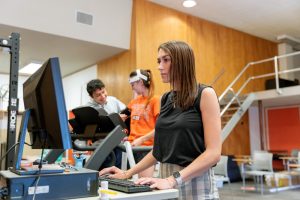 A photo of a researcher with a machine hooked up to a student on a workout machine.