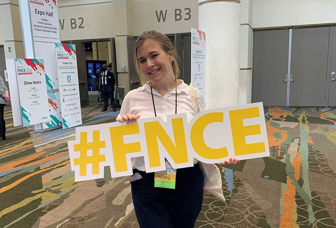 Maddy Baker standing with the letters FNCE in front of her