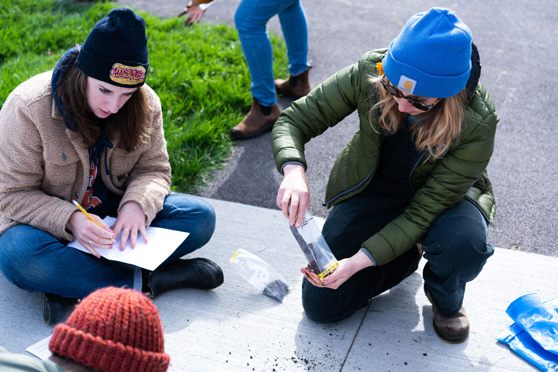 Two students are on a patio examining something and taking notes