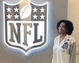 Alumna Angela Marsh-Coan stands in front of a NFL logo wall decal.