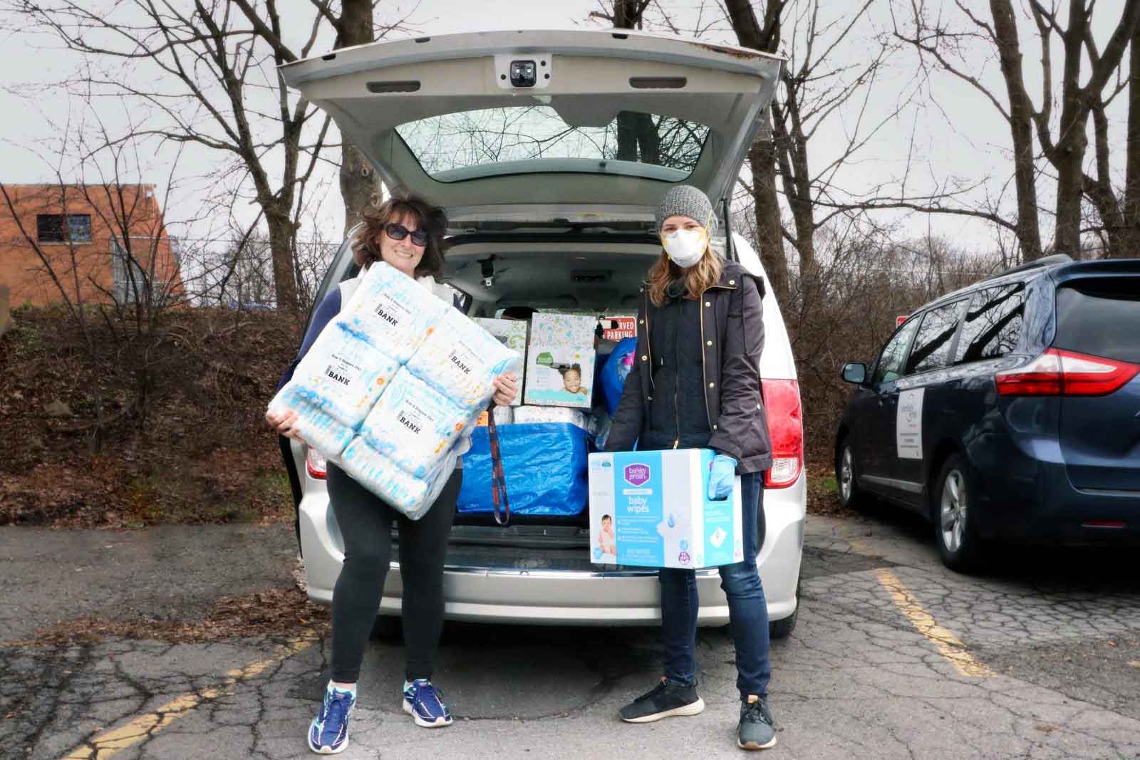 Two women are taking boxes of diapers out of the back of a car