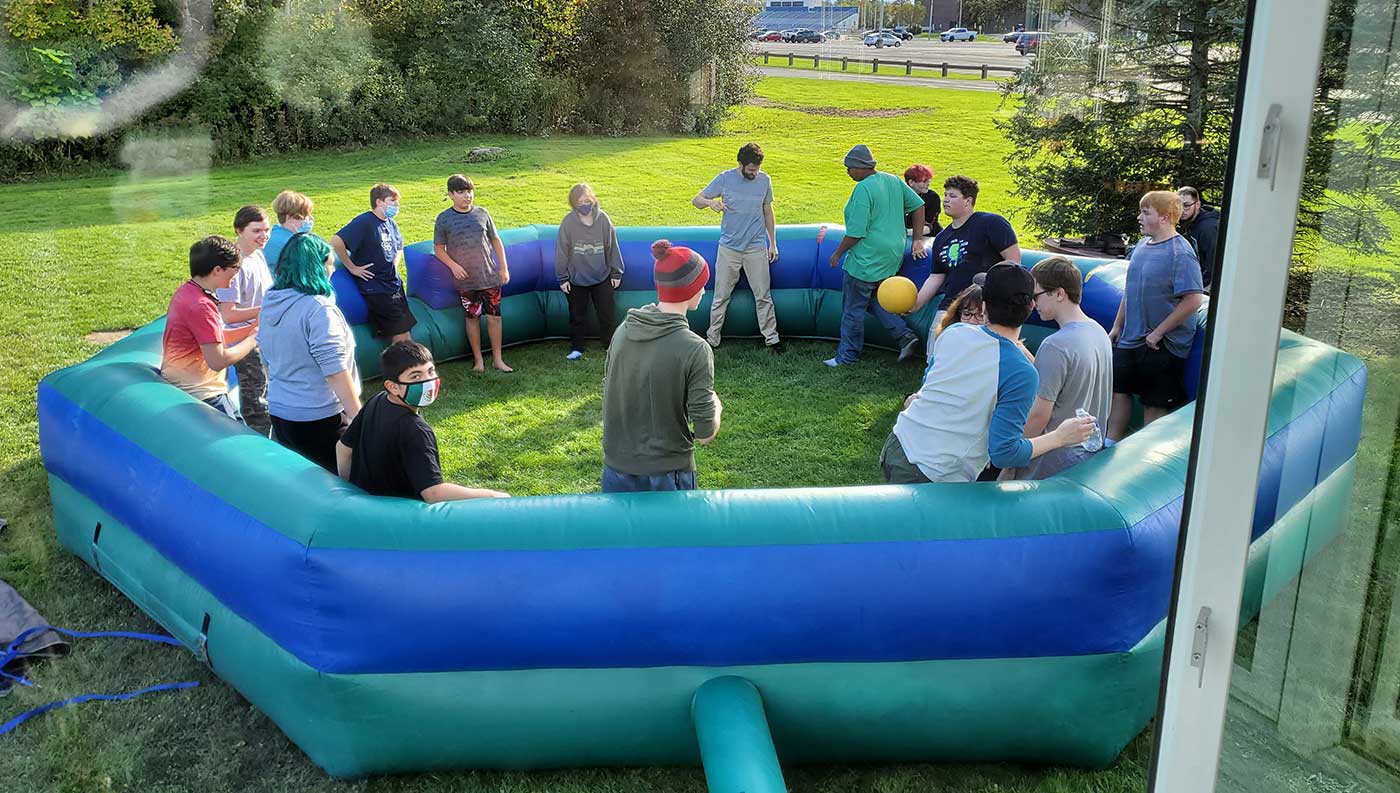 A number of teens are inside a large blow up pool playing a game