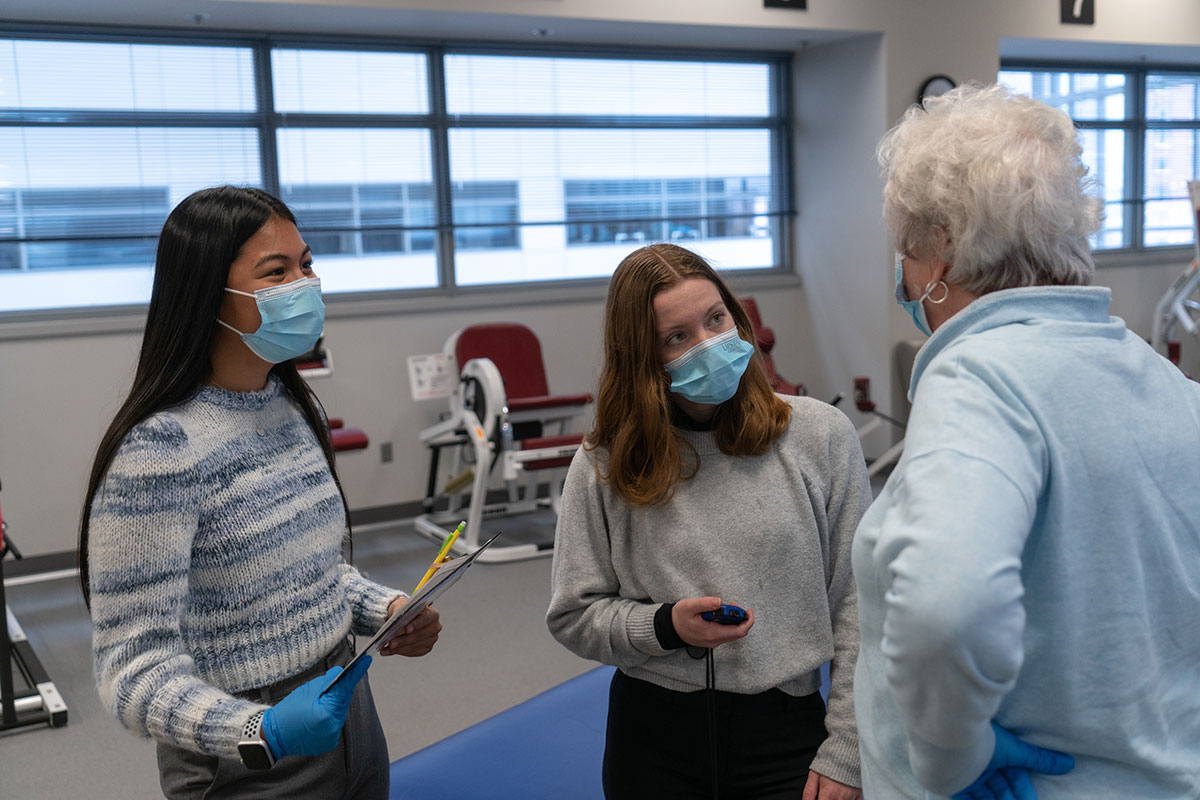 Two students talk with an older person in a lab.