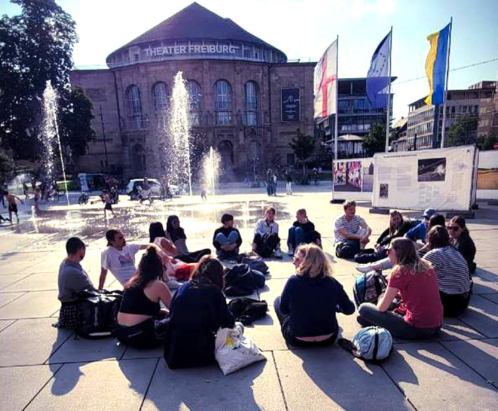 A group of persons are sitting in a circle in a commons.