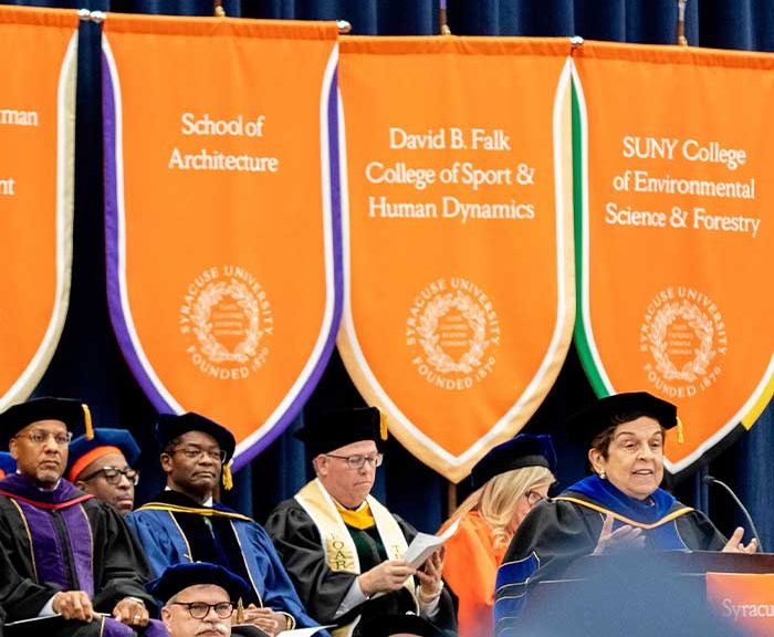Professors sit behind a commencement speaker at a graduation ceremony