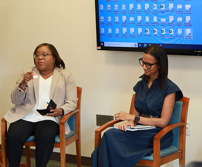 two woman sitting in front of a screen presenting