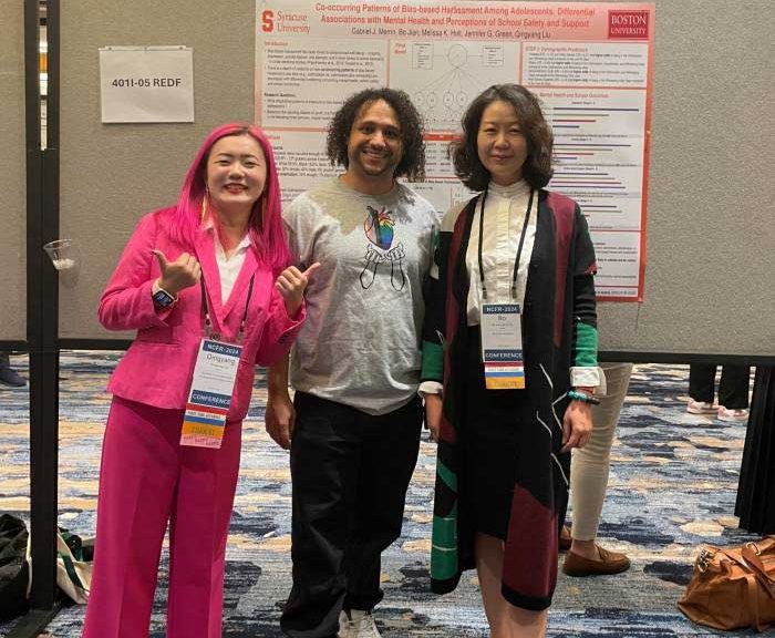 Three persons are posed in front of a conference poster