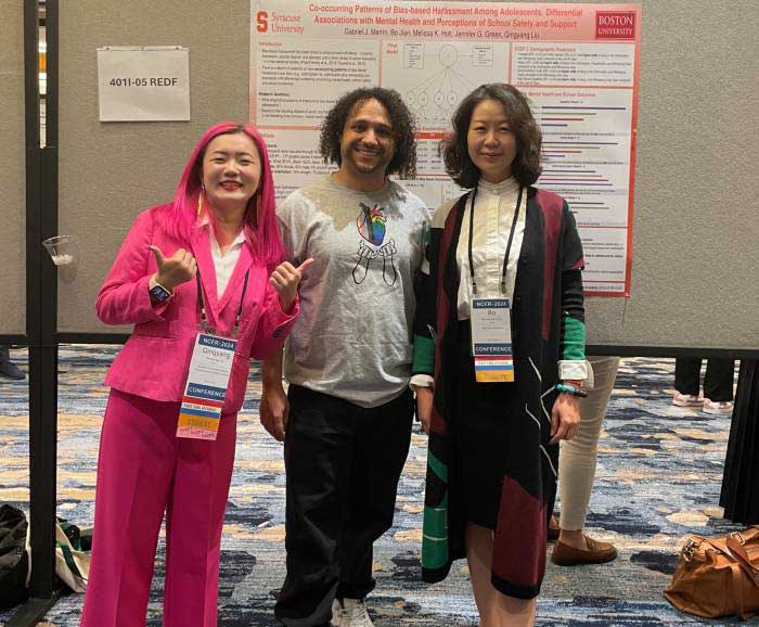 Three persons are posed in front of a conference poster