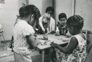 Four little girls and a boy play with a teacher at a table