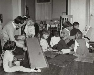 A classroom with children reading together while a teacher helps a child down a small slide