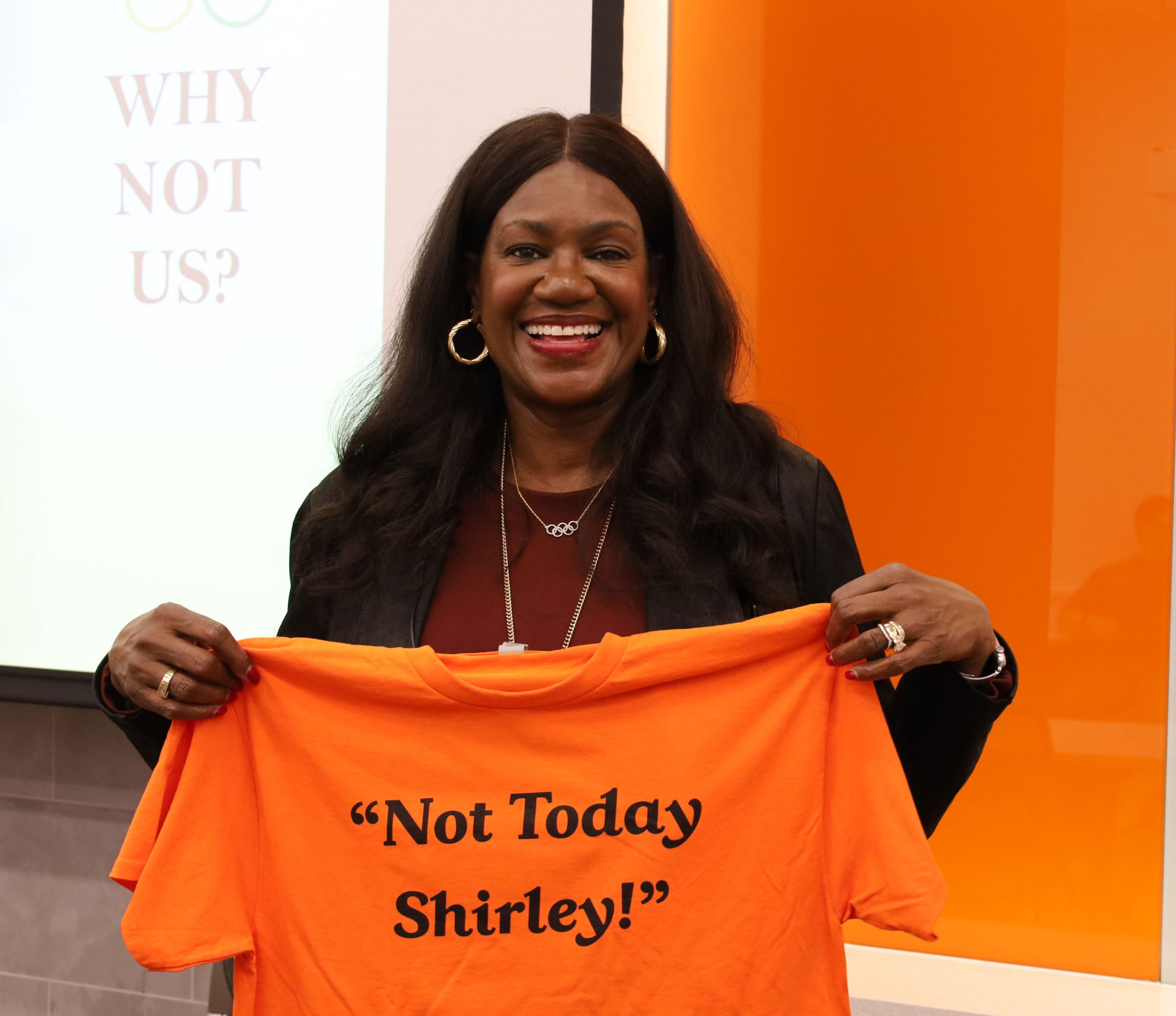 Women with long dark hair holding up orange t-shirt that says Not Today Shirley