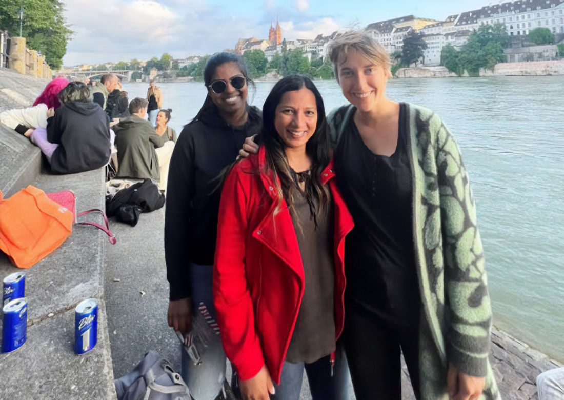 A group of three individuals are posed together at a riverfront