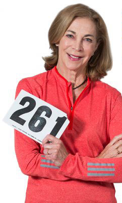 A woman smiles while holding up her number 261 Boston Marathon bib. Kathrine Switzer