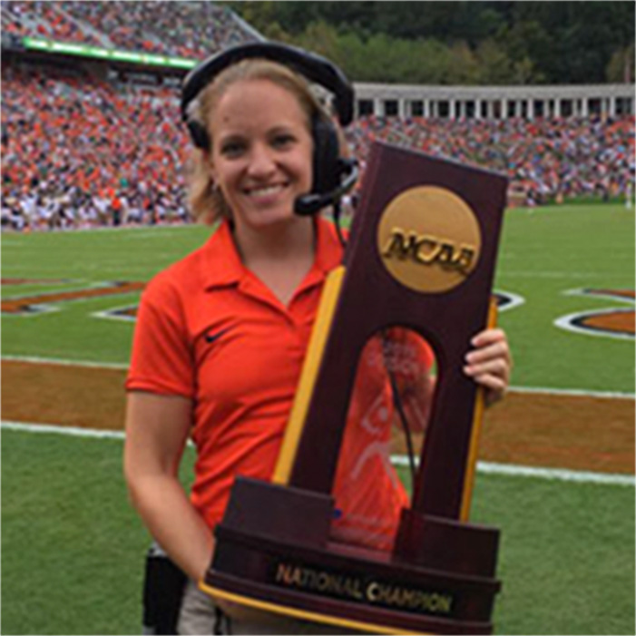 Katie Rudy during an American football game holding a NCAA trophy