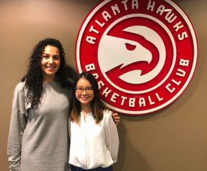 Alumna Blake Johnson with graduate student Cherie Hong standing in front of the Atlanta Hawks logo