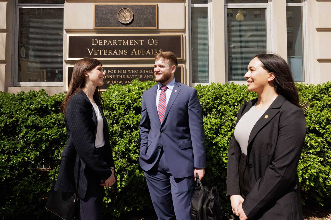 Three students talk in front of a Veterans building.