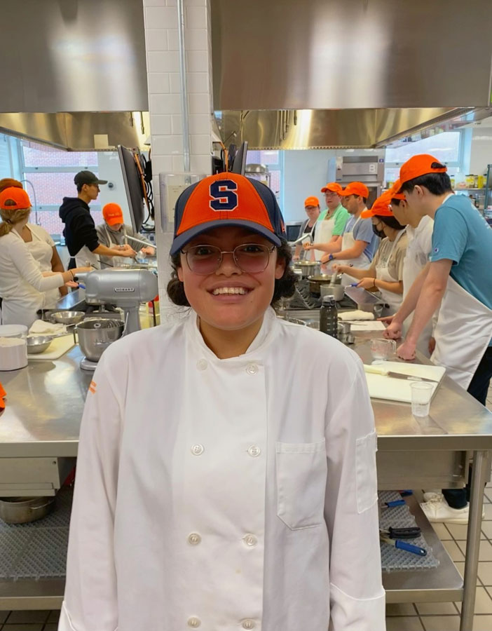 April is standing in a professional kitchen with other students behind her.