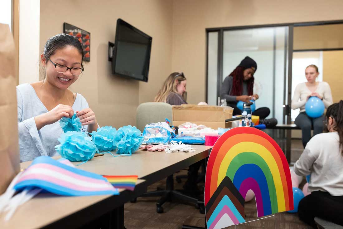 Students work build colorful paper items at a long table.
