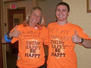A couple wears shirts that say I'm his/her C.E. partner, think happy be happy