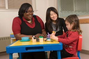 Two students work with a child at a table of toys