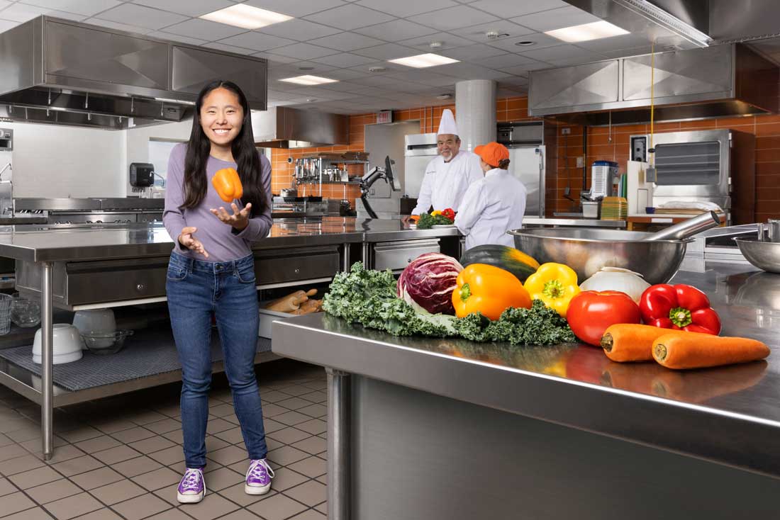 Photo of Mackenzie Gleason in a test kitchen, catching a bell pepper midair.